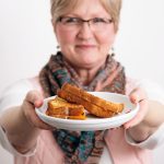 A woman holding out a plate of grilled cheese sandwiches.