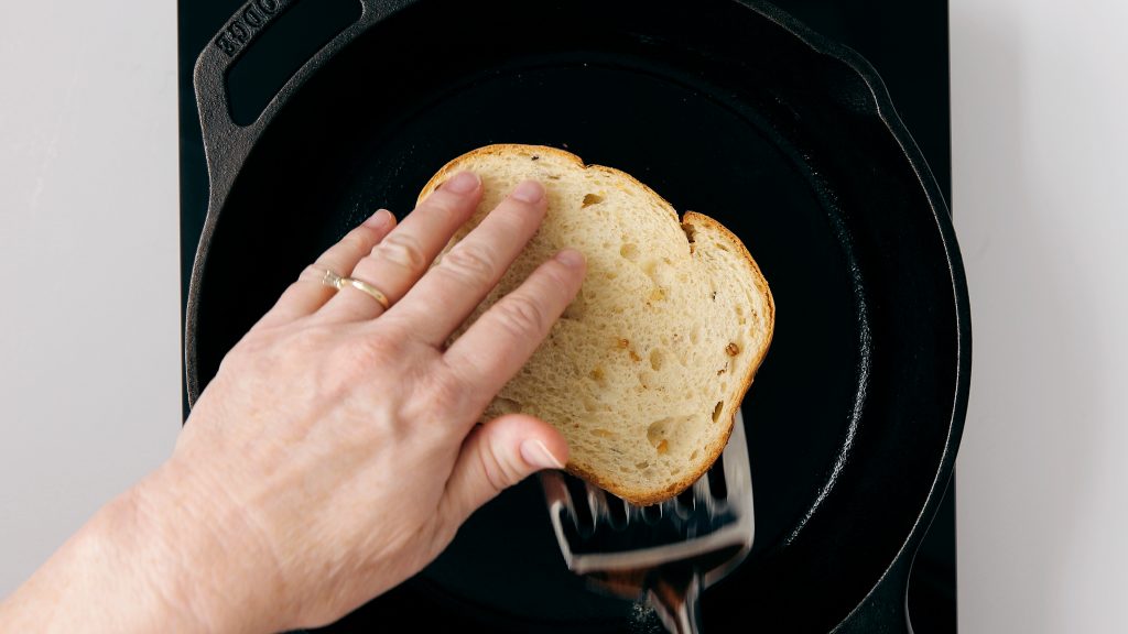 Flipping a grilled sandwich with a spatula on a cast iron skillet.