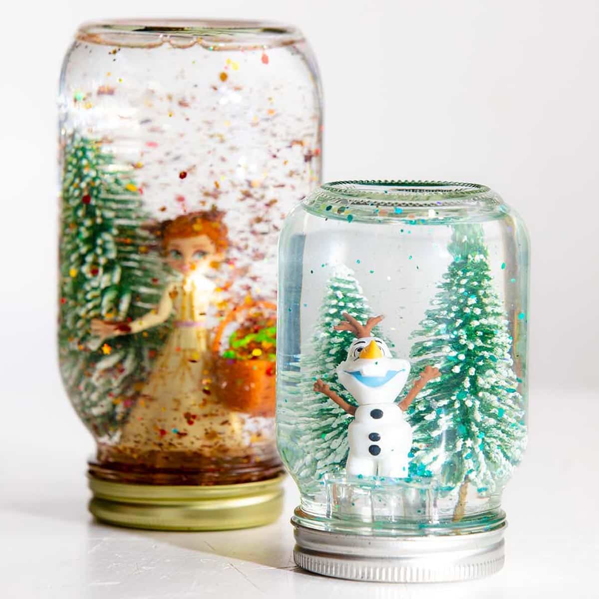 Two mason jar snow globes with trees and Olaf and Anna Frozen characters.