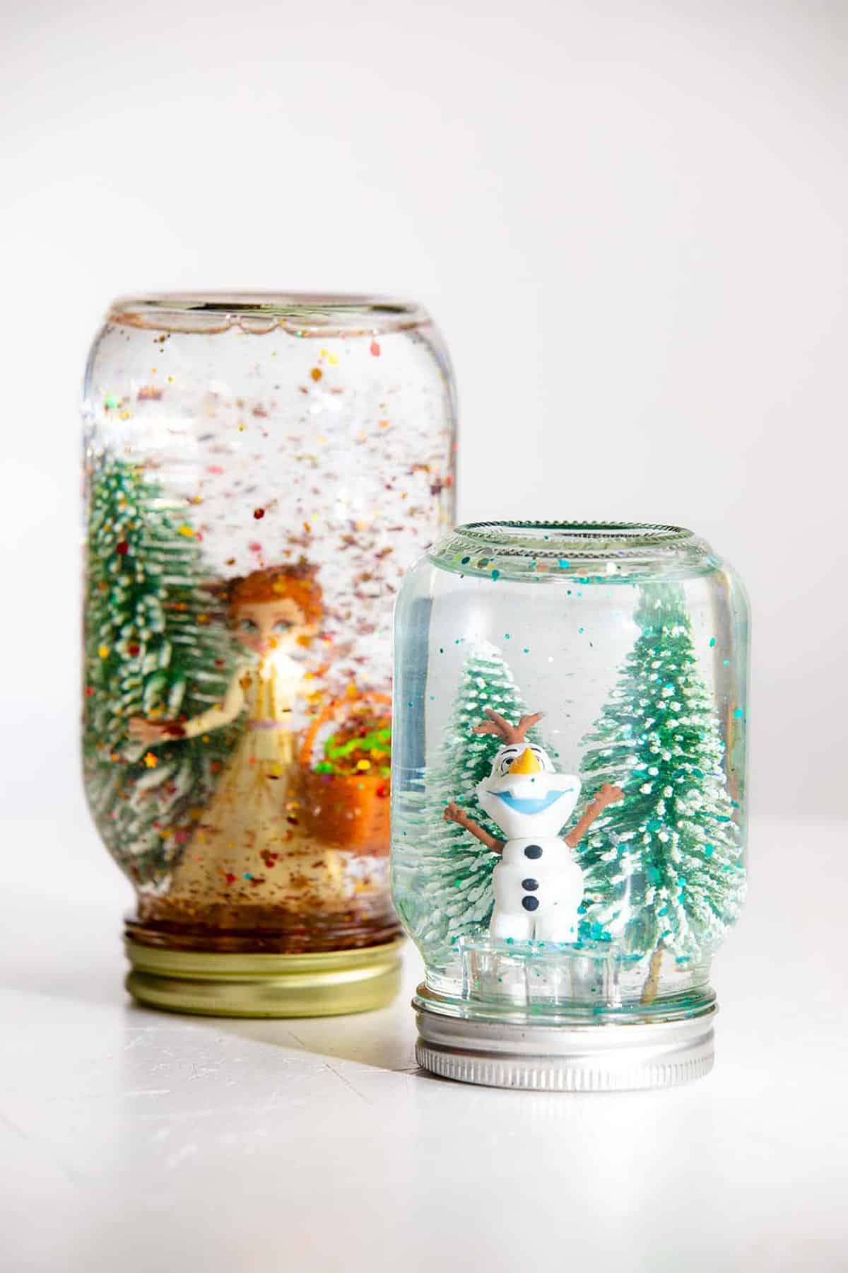 Two mason jar snow globes with trees and Olaf and Anna characters.