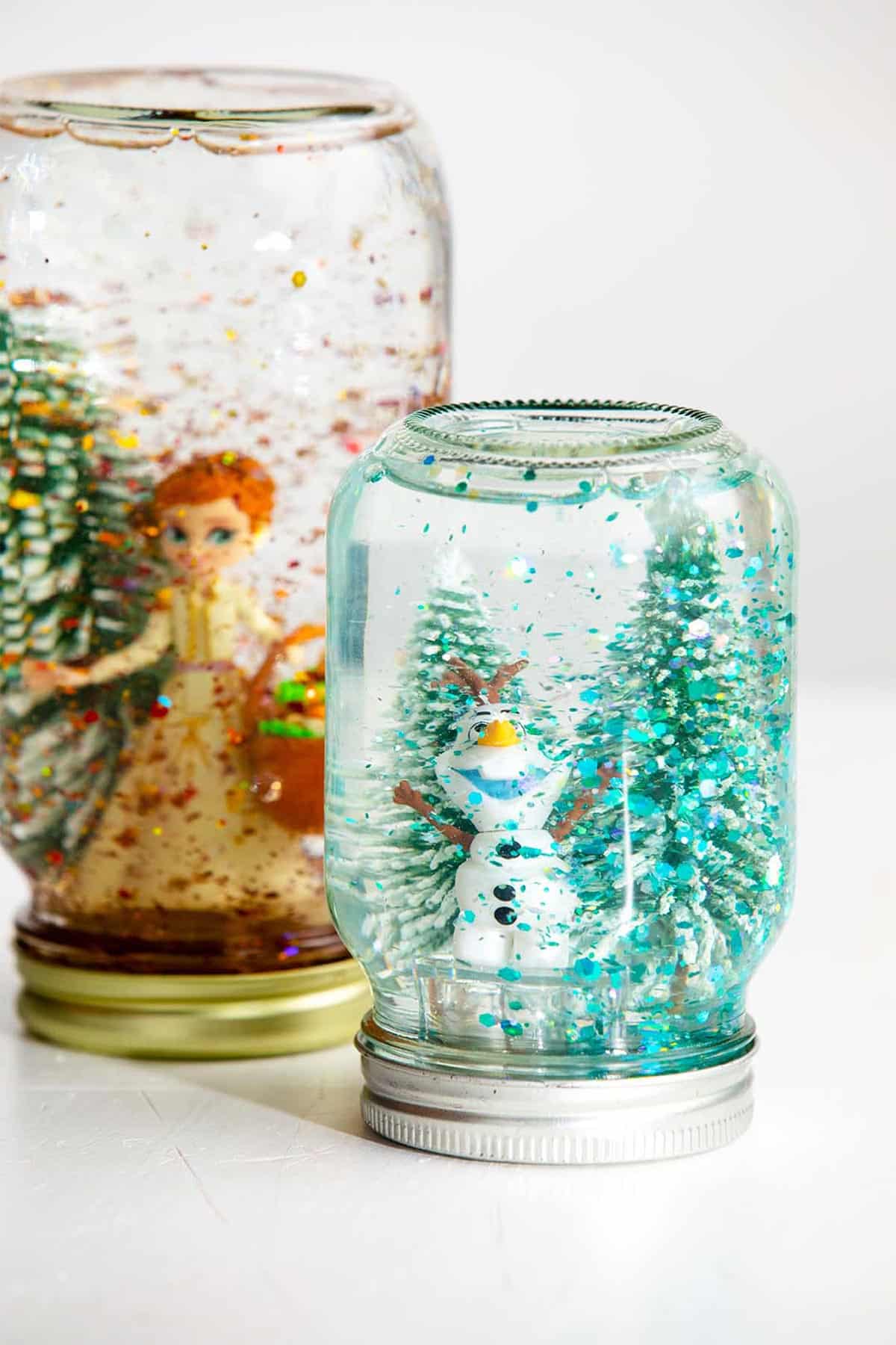 Two mason jar snow globes with trees and Olaf and Anna characters.