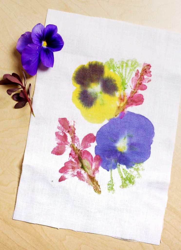 A colorful print of hammered flowers on fabric, a purple flower nearby.