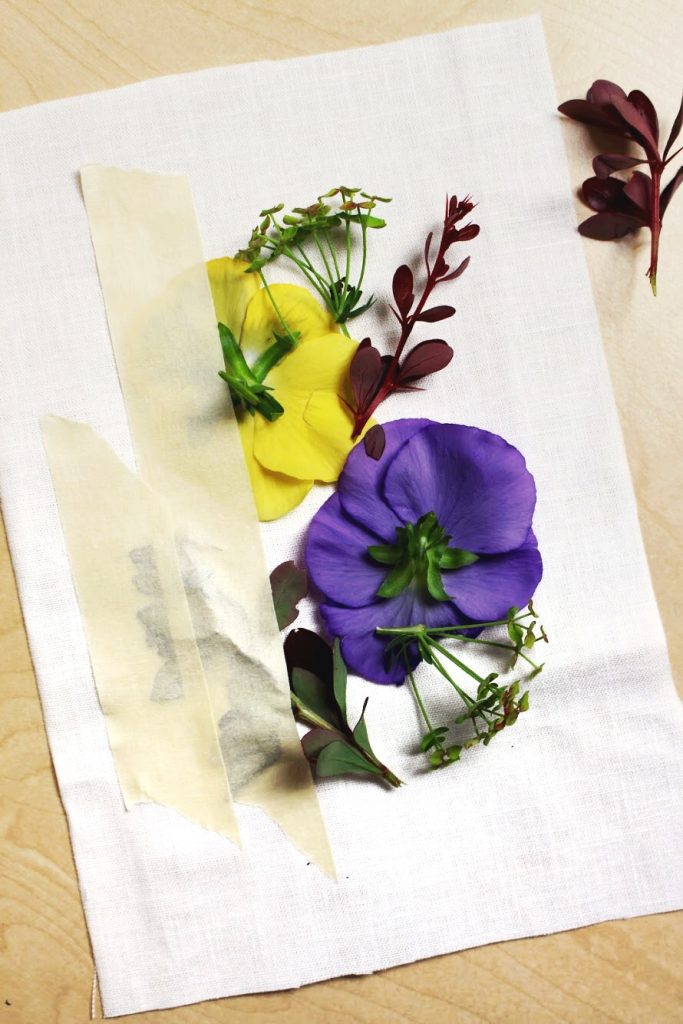 Purple and yellow flowers taped to a piece of white fabric.