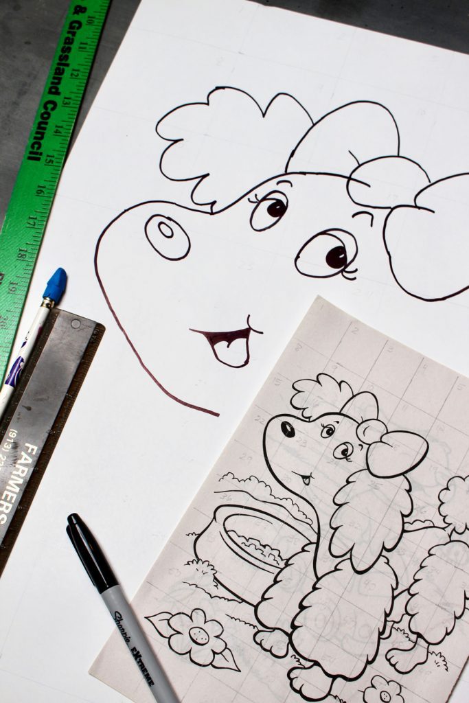 A puppy cartoon character being drawn onto a posterboard from a guide.