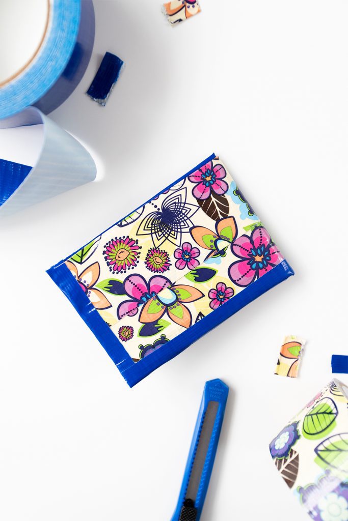 A flower patterned duct tape wallet, utility knife and blue roll of duct tape.