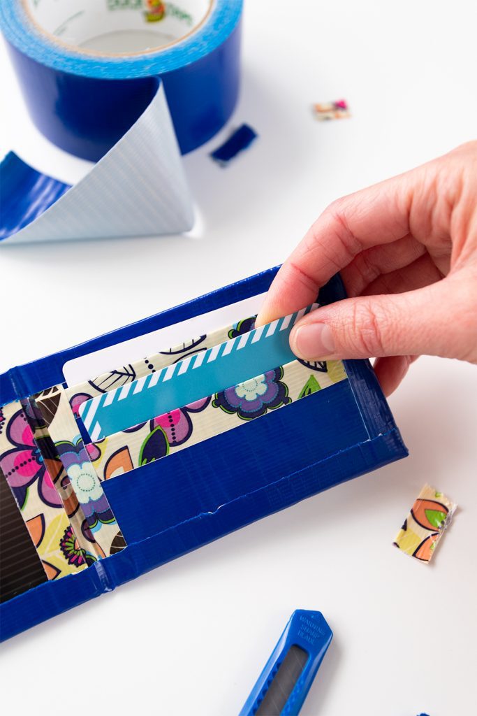 Adding a card to the pocket of a duct tape wallet, blue duct tape roll in the background.