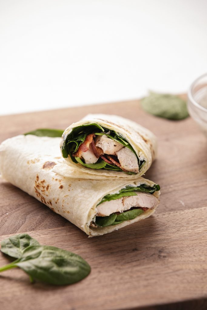 A turkey wrap with spinach and bacon on a cutting board.