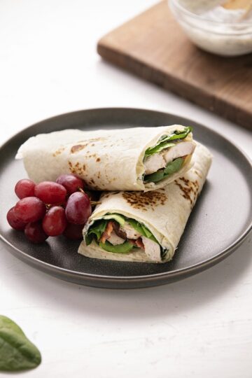 A turkey wrap with greens and bacon on a plate with grapes.