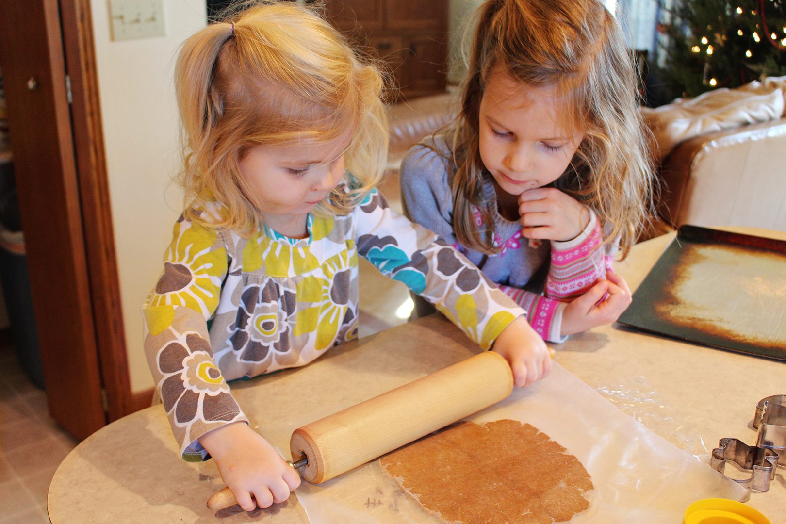 Two children using a rolling pin to roll out gingerbread dough between two pieces of wax paper.