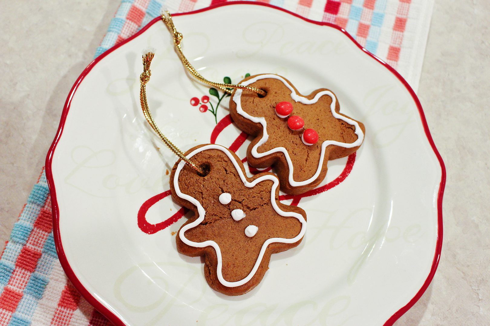 Two gingerbread men cookies decorated with white icing and red hot candies sitting on a Christmas plate.