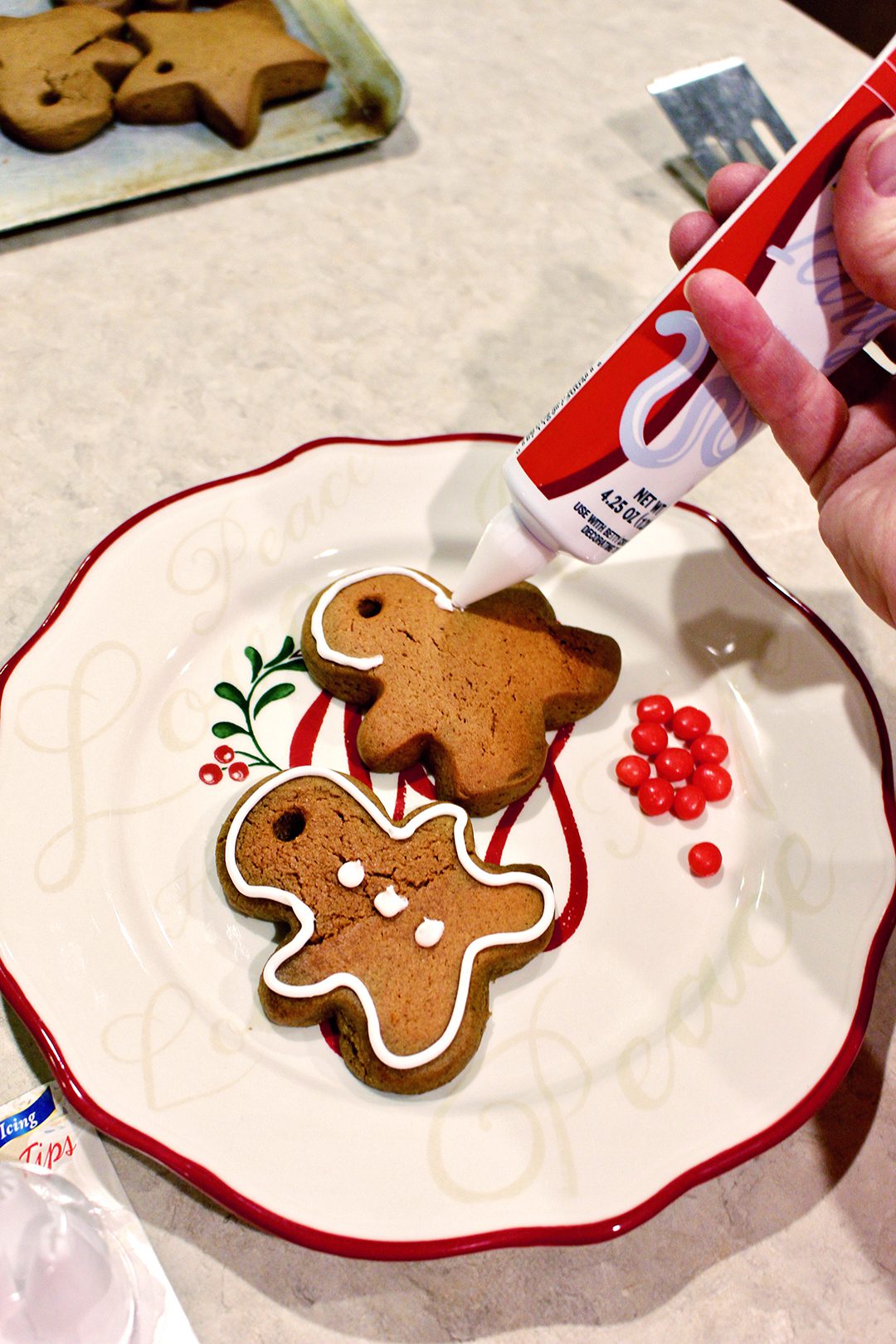 Adding icing from a piping container to gingerbread cookies on a Christmas plate.