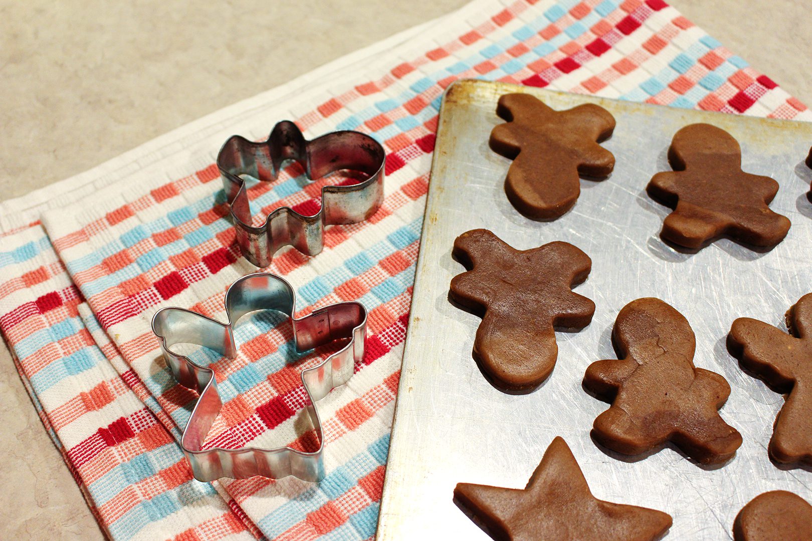 Gingerbread cookies arranged on a baking sheet nearby some cookie cutters on a linen.