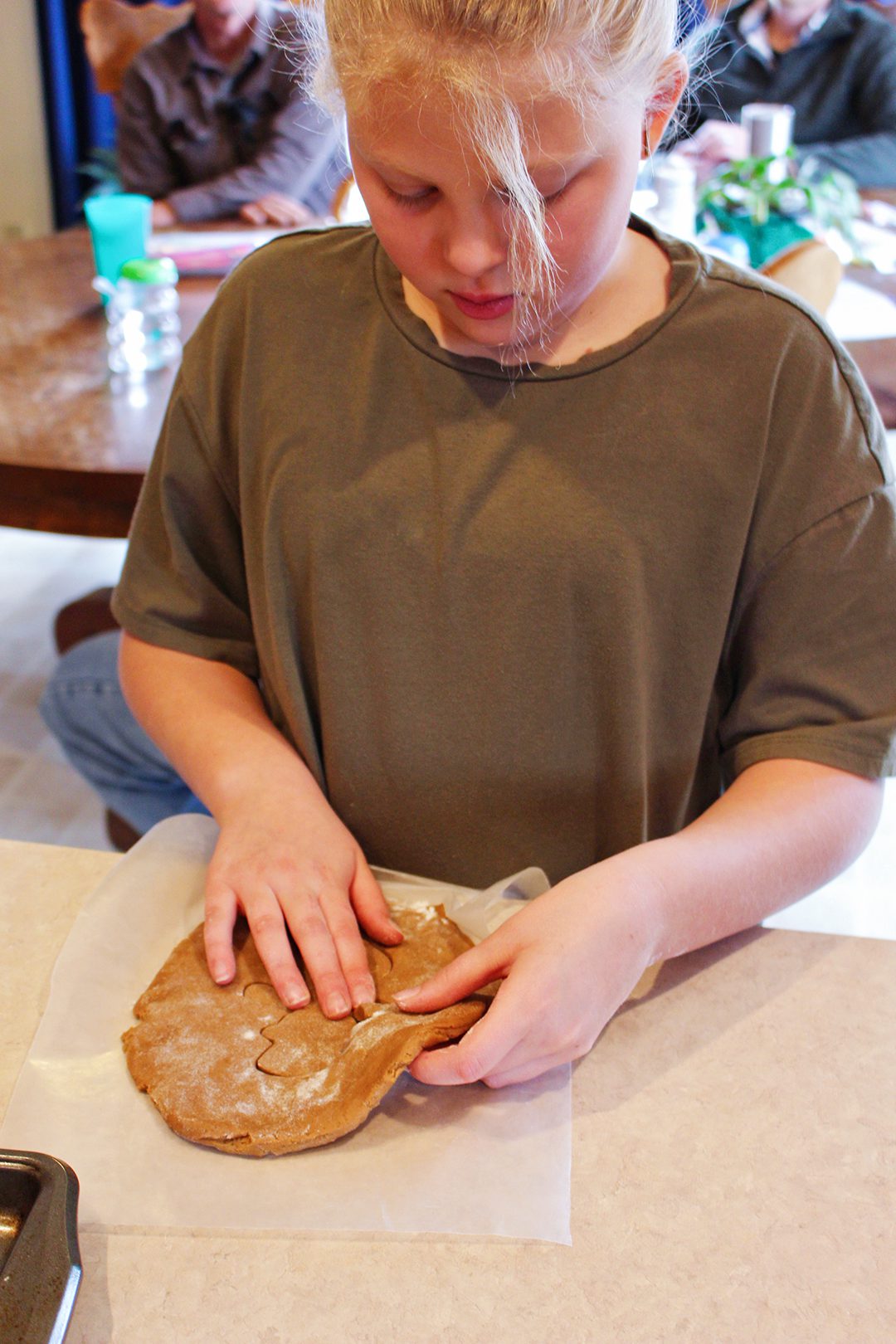 A girl cutting a snowman shape out of gingerbread dough.