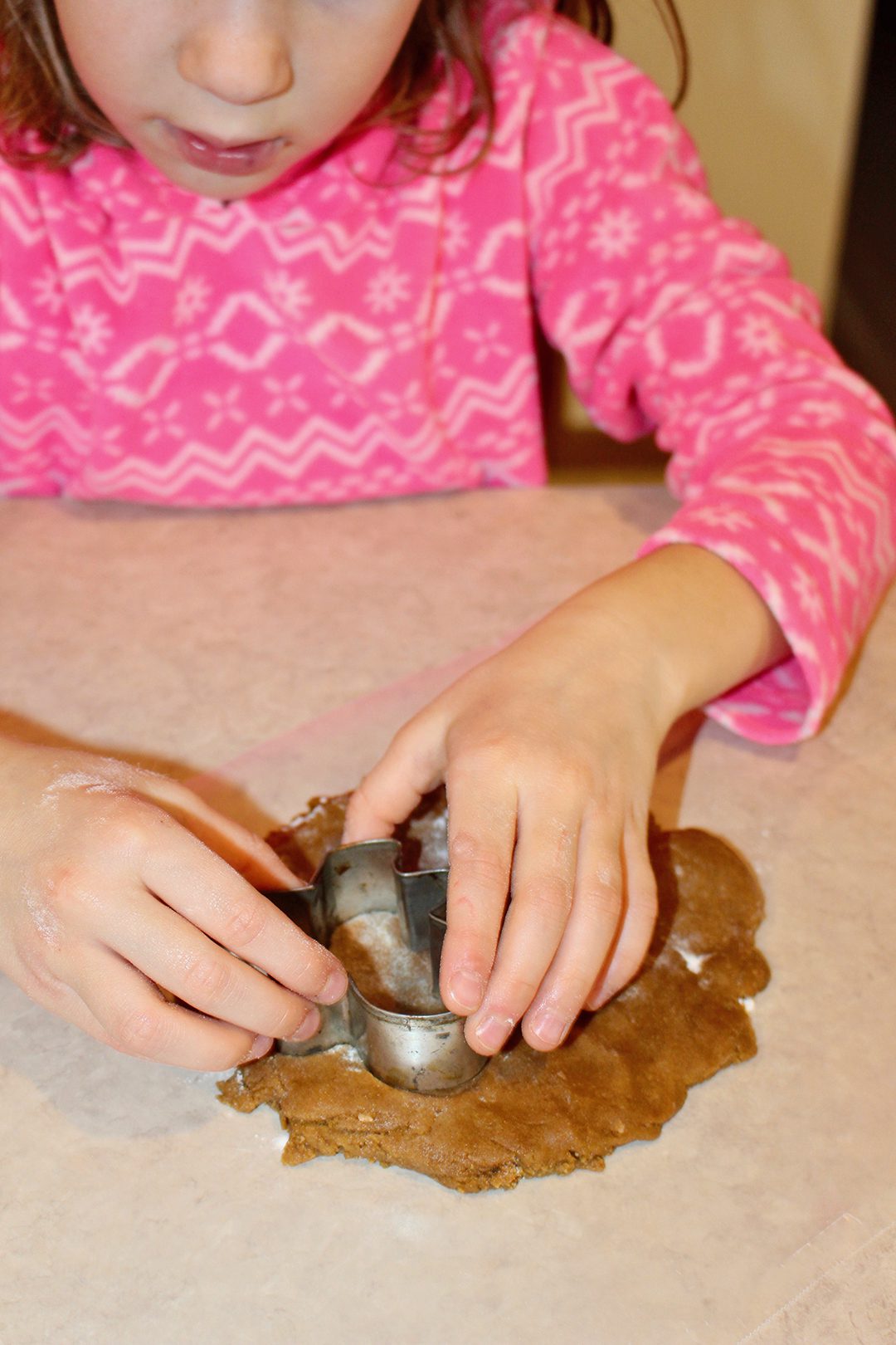 A girl cutting a gingerbread man shape out of some gingerbread cookie dough.