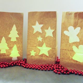 Three brown paper bags with Christmas shapes cut out, glowing from a candle inside