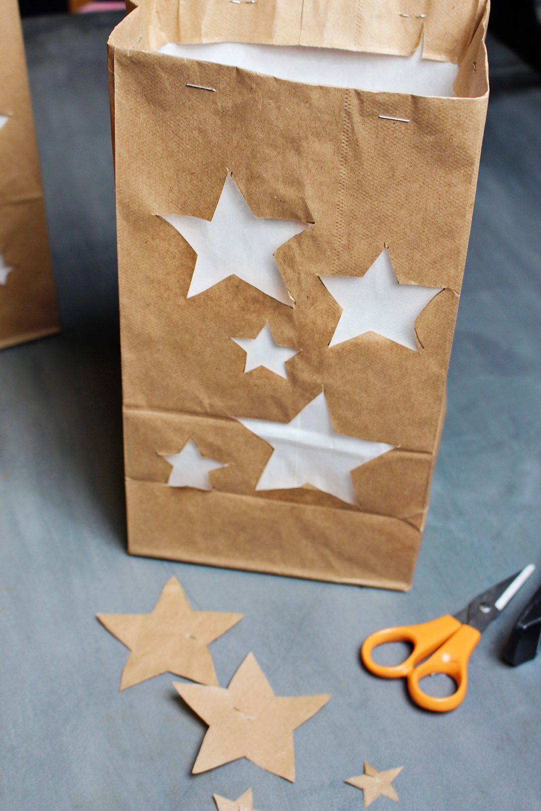 A brown paper bag with stars cut out from the front, lined with white paper, near a pari of scissors.