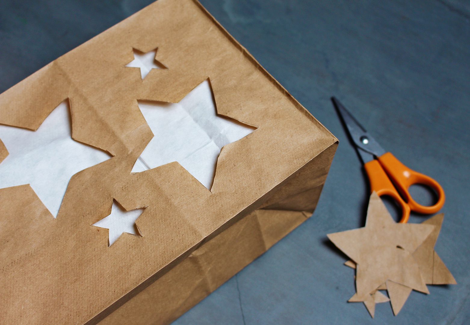 Stars cut out of a brown paper bag lined with a white paper lunch bag, near a pair of scissors. 