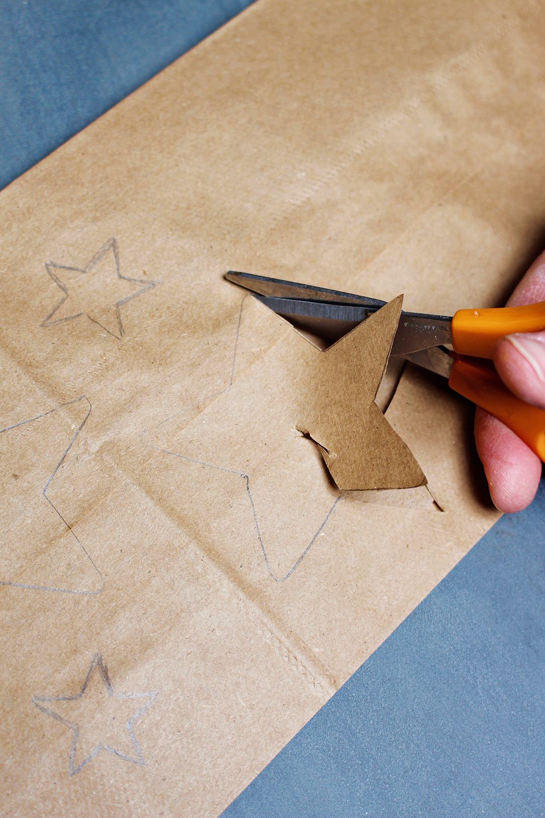 A pair of scissors cutting out star shapes from a brown paper bag.