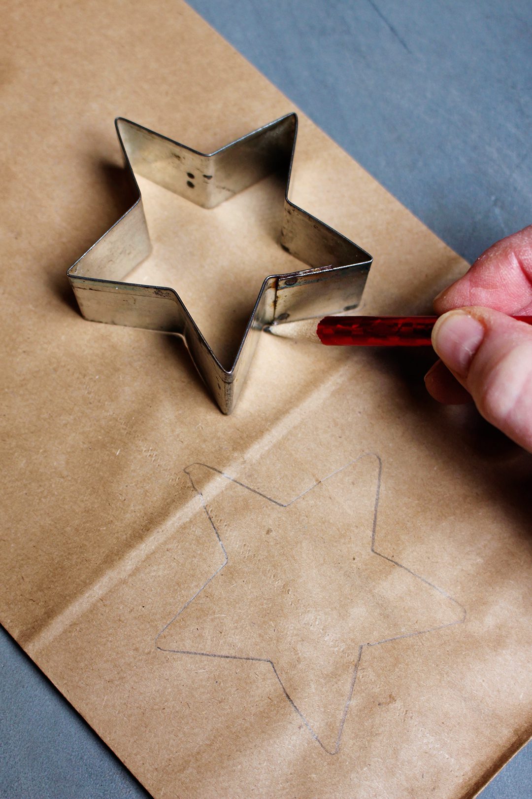A pencil tracing around a star shaped cookie cutter on a brown paper bag.