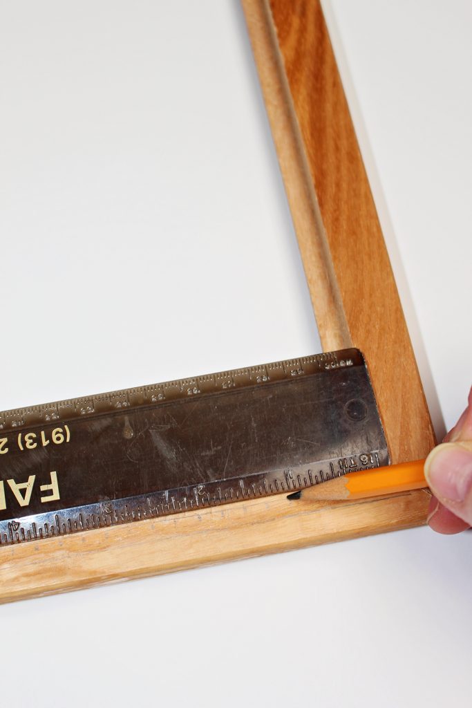 A pencil marking measurements from a ruler along a wooden picture frame.