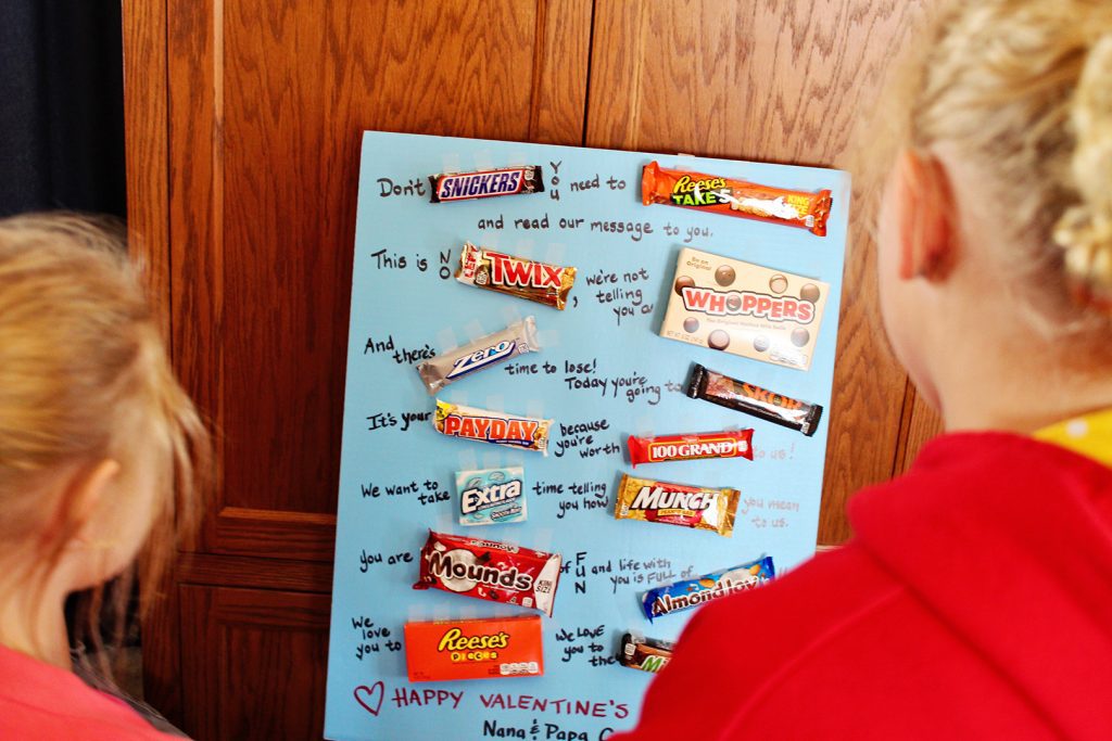 Children reading a poster board Valentine card with candy on it.
