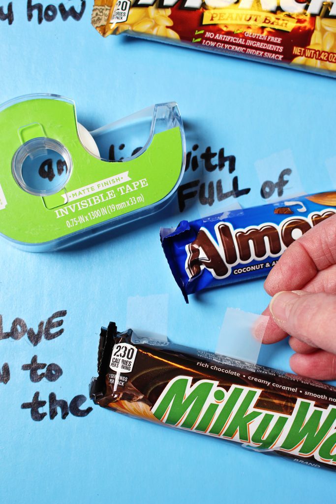 Scotch tape, Almond Joy candy bar, and a Milky Way candy bar being taped to a poster board.