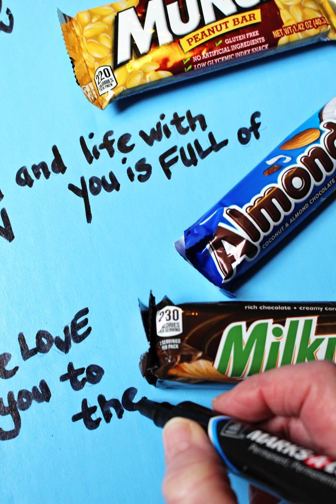 A sharpie writing a message on a poster board with candy bars around it.