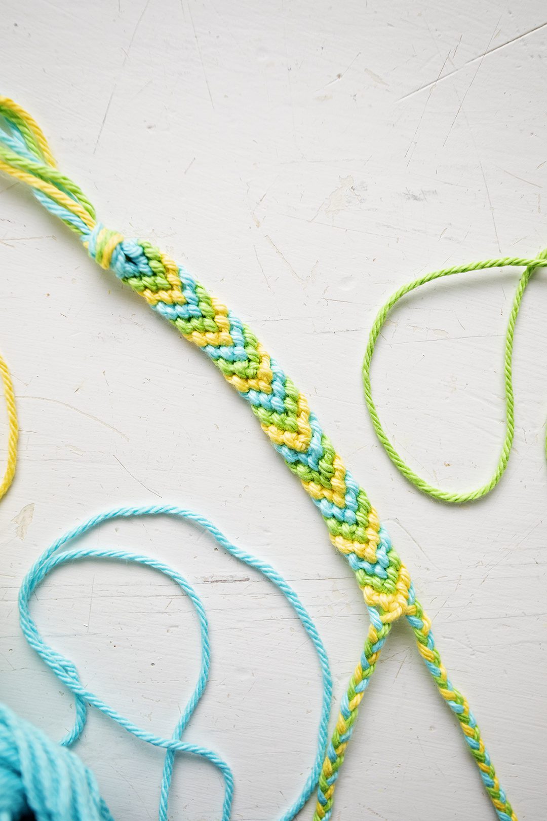 A chevron pattern bracelet made from blue, green, and yellow string.