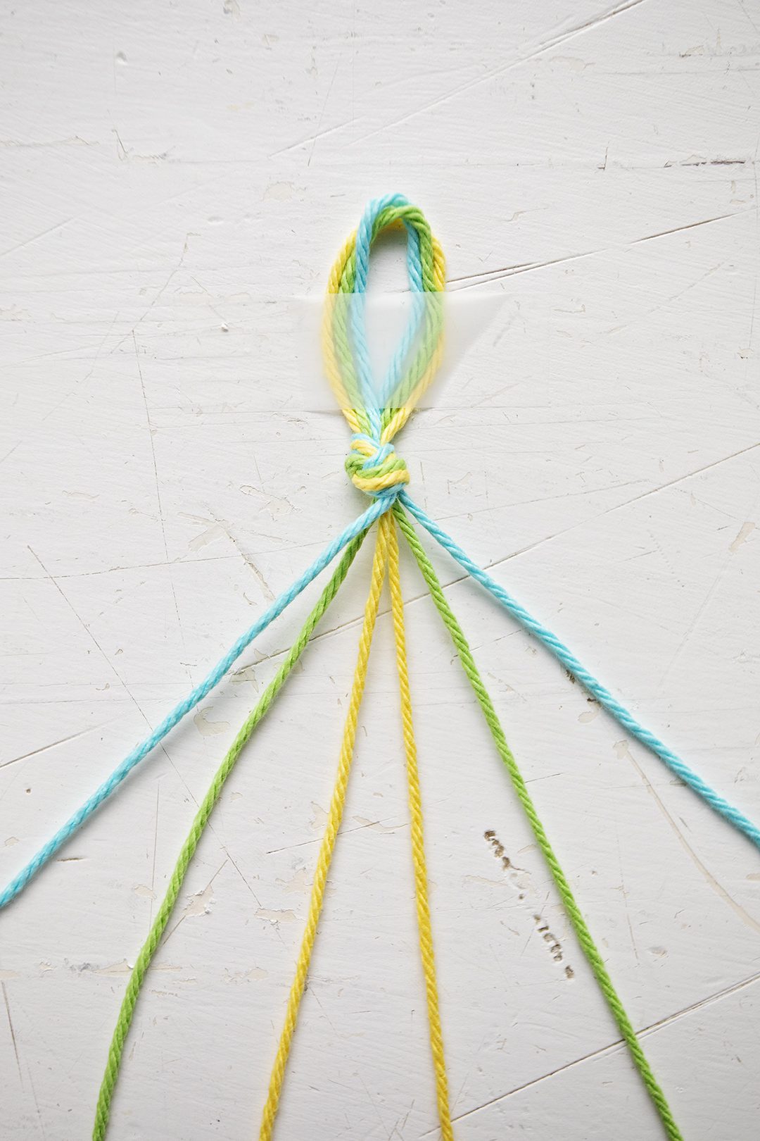 A chevron pattern bracelet being made from blue, green, and yellow string.