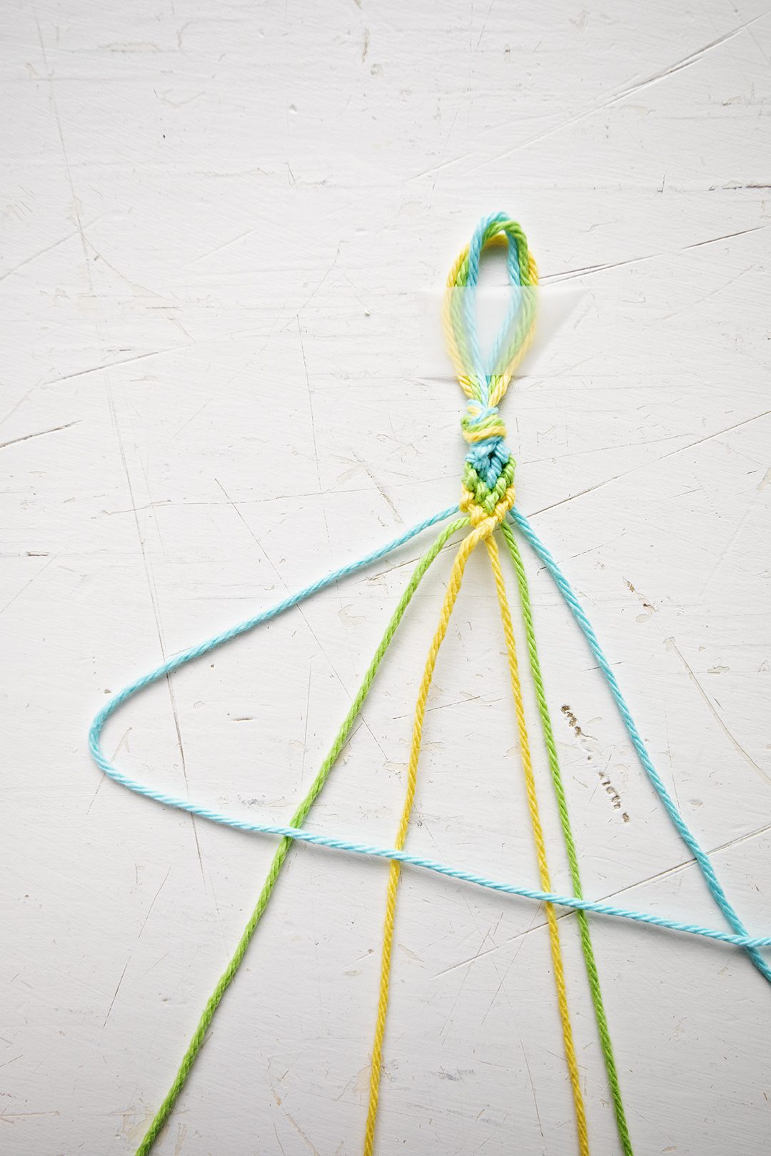 A chevron pattern bracelet being made from blue, green, and yellow string.