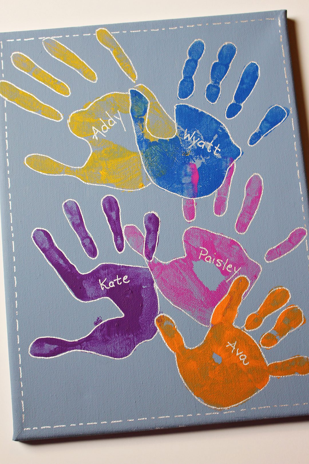 Painted handprints on a canvas with names written on them.