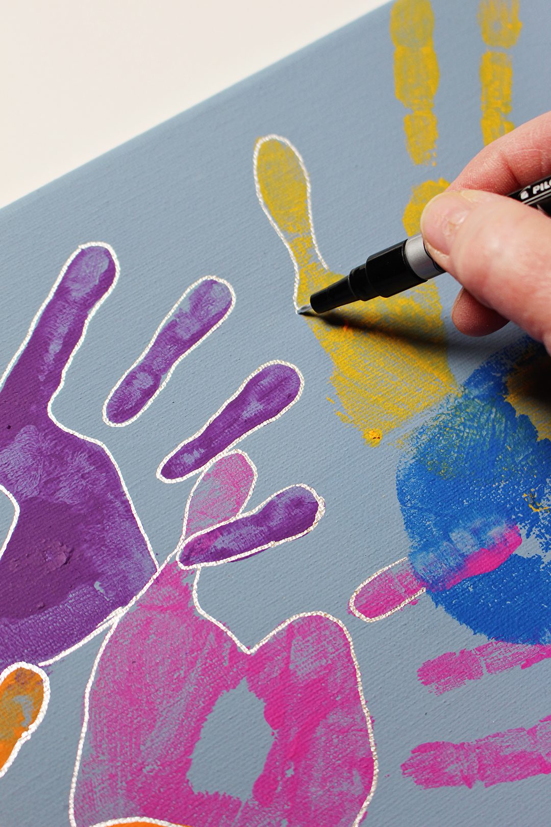 An outline being drawn around painted handprints on a canvas.
