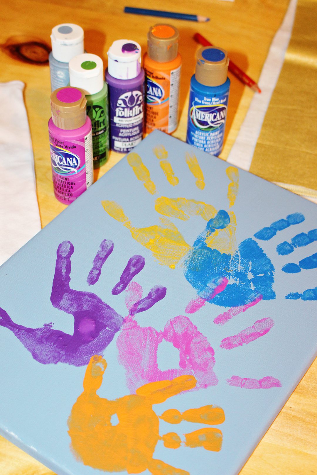 Colorful handprints on a canvas with paint tubes nearby.