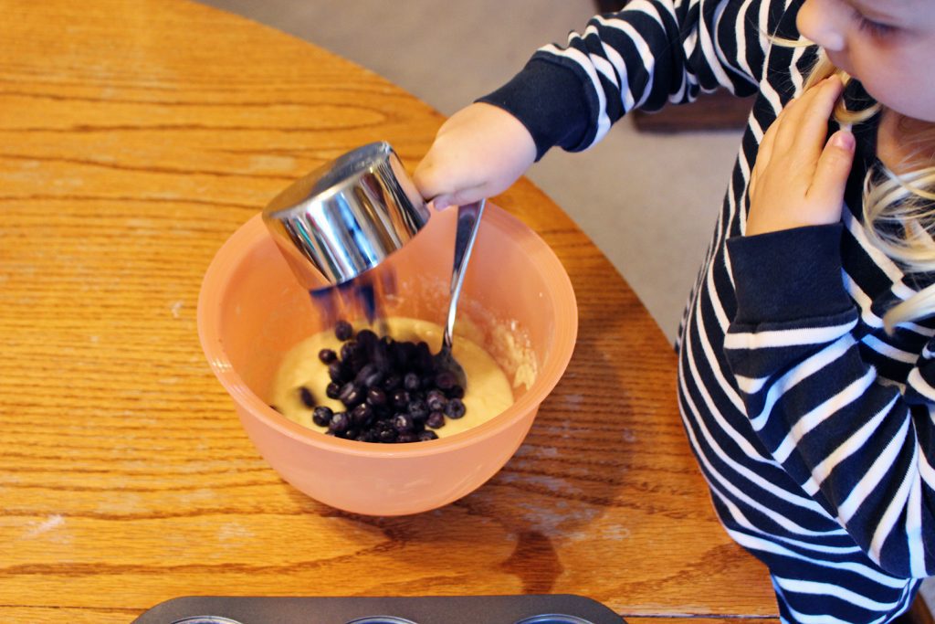 A child pouring blueberries into donut batter.