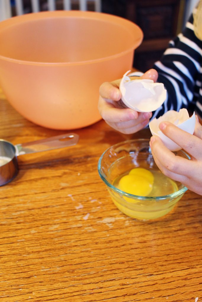A child breaking an egg into a small bowl