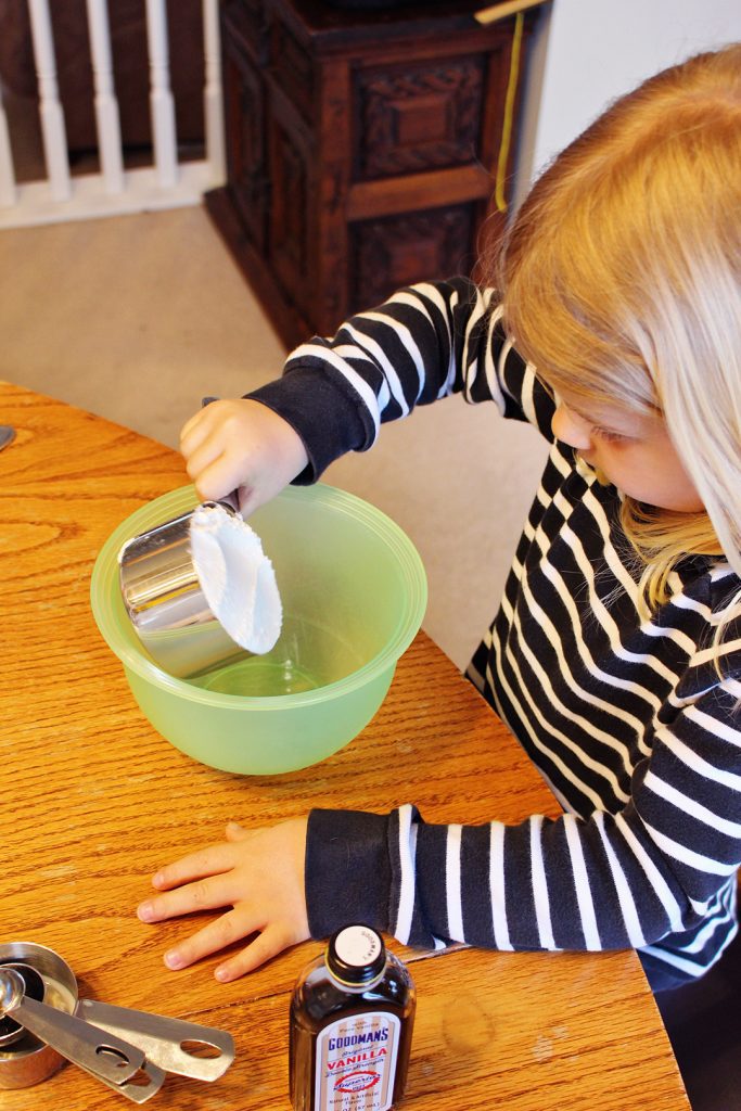 A child adding powdered sugar to a bowl.