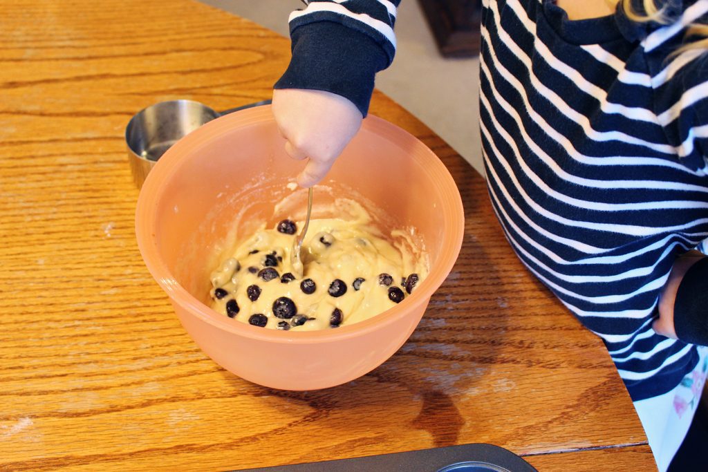 A child mixing blueberries into donut batter.