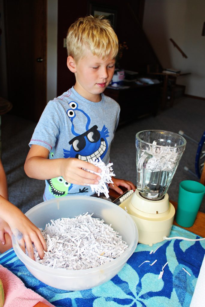 A child adding shredded paper to a blender with water.