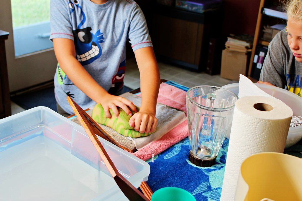 A child pressing a sponge over a wet piece of recycled paper.