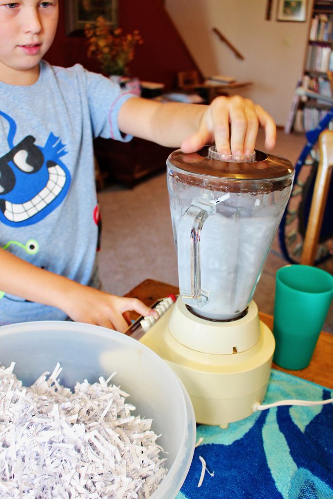 A child blending paper scraps in a blender with water.