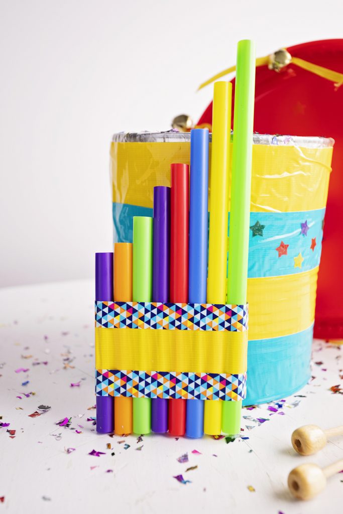 A fife made from colorful straws sitting against a striped can drum.