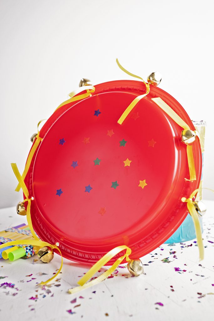 A red tambourine made from plates with bells, yellow ribbon, and stickers.