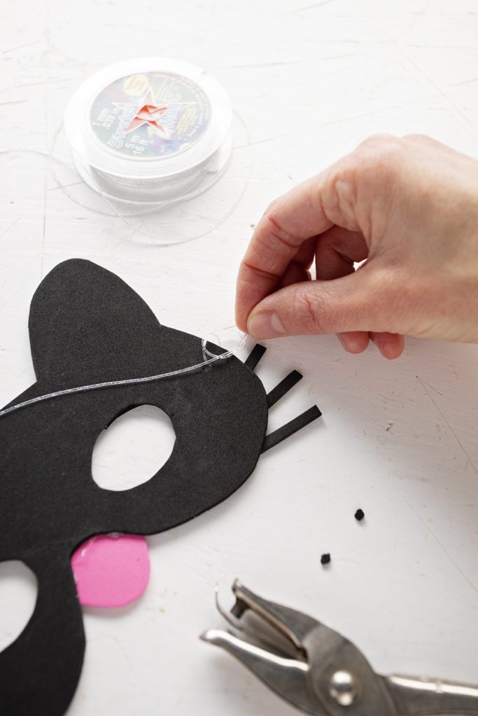 Tying elastic string to the side of a craft foam cat mask.