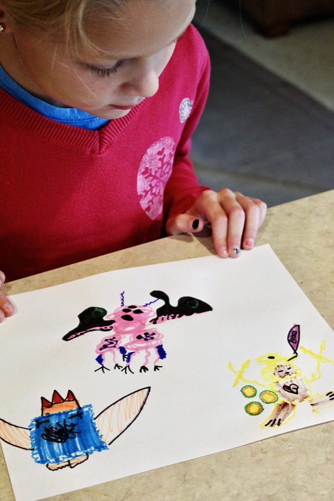 A child looking a t apiece of paper with scribble monsters colored from markers.