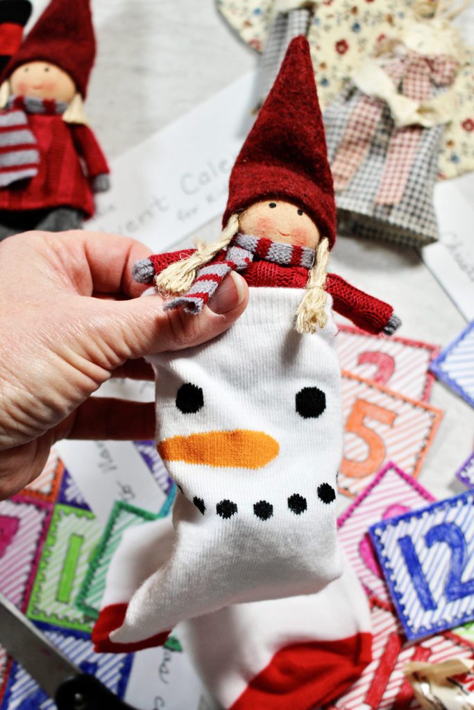 Doll being placed in a Christmas sock to hang on the tree, advent calendar numbers in the background