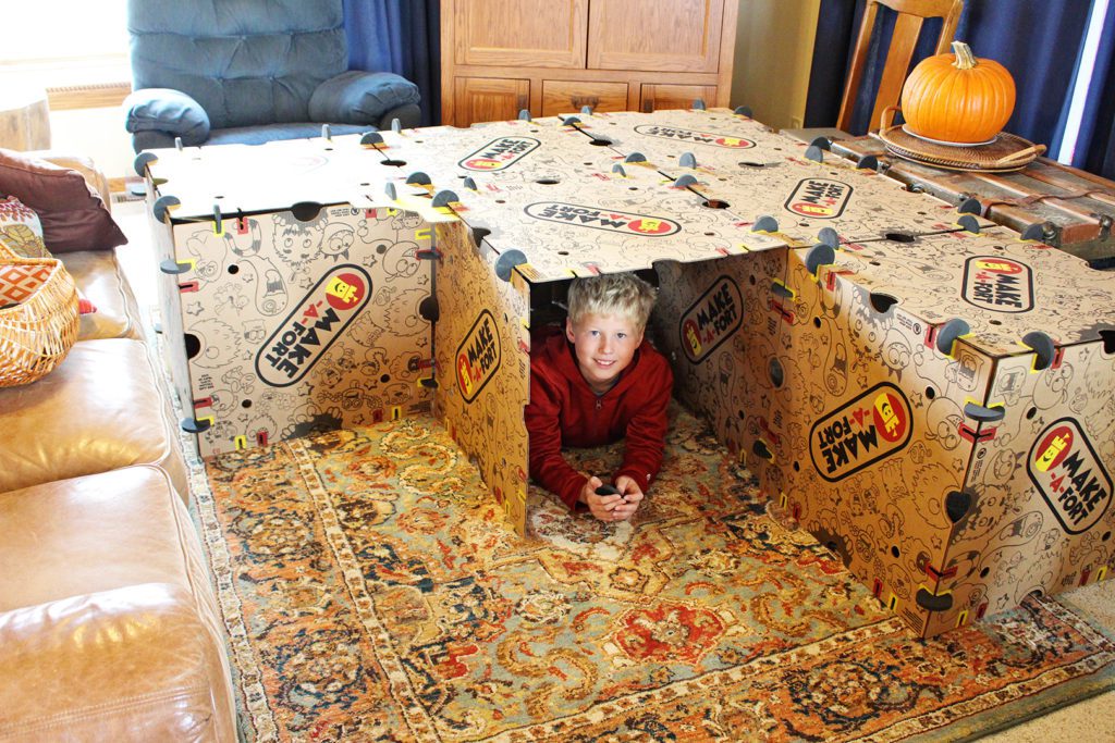 A boy playing inside his living room fort from the Make-A-Fort kit