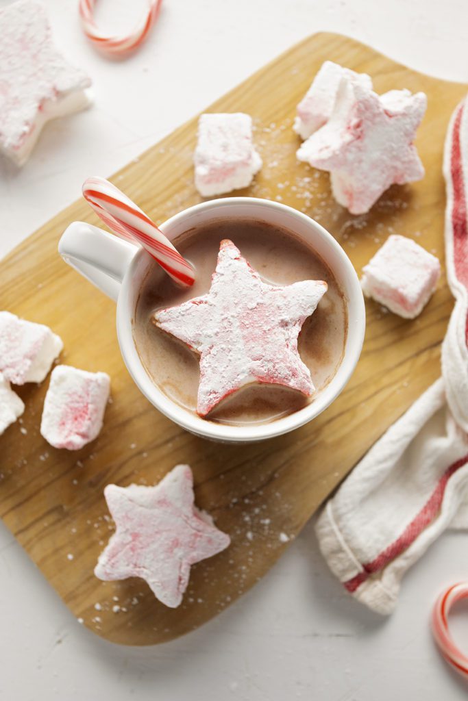 Star shaped peppermint marshmallows in a mug of hot chocolate with a candy cane.