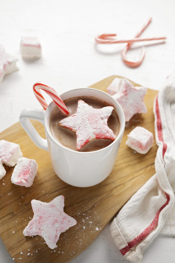 Star shaped peppermint marshmallows in a mug of hot chocolate with a candy cane.