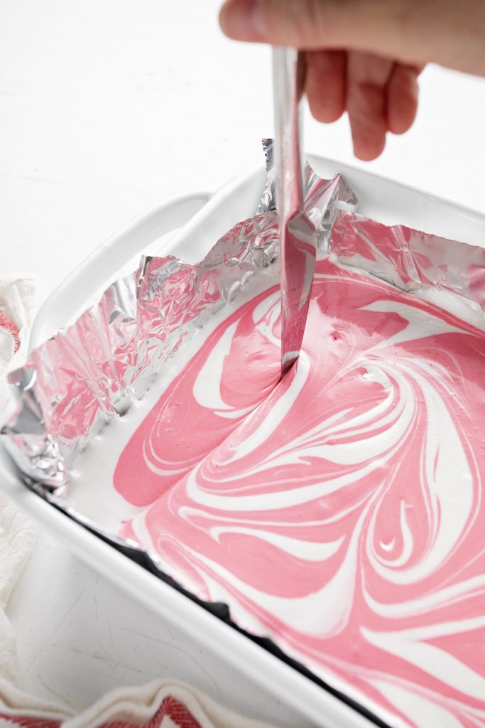 A knife swirling the pink and white marshmallow fluff in a baking dish.