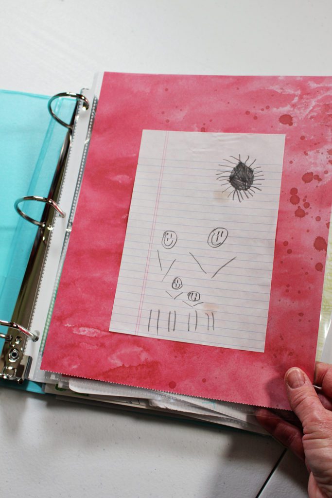 A child's pencil drawing of a family and sun on a page in a binder.